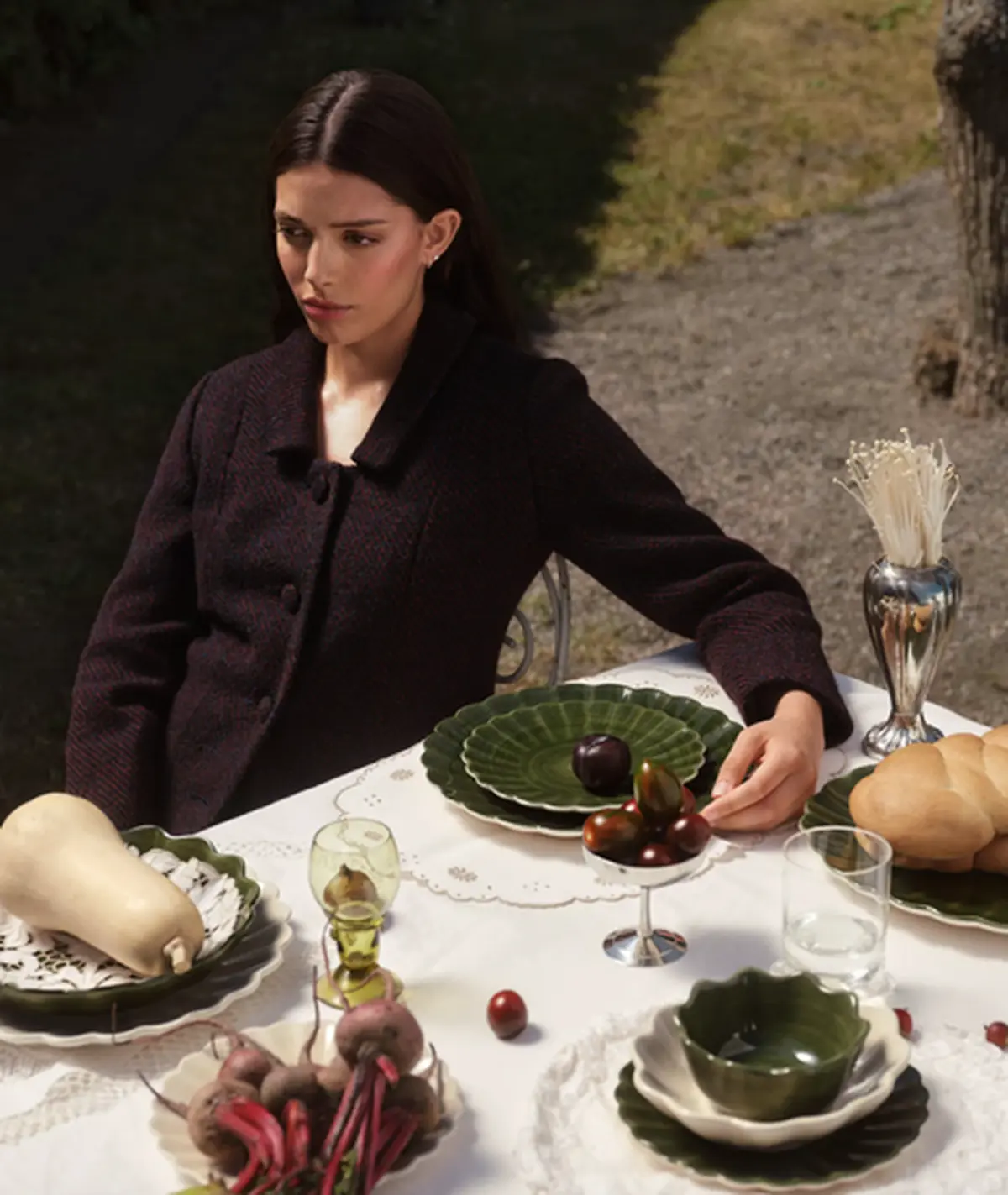 Woman seated at a set dinner table outdoors with green ceramic plates